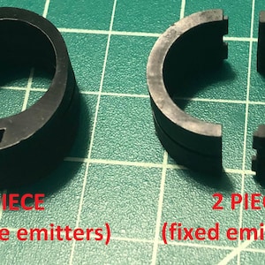 K&ouml;nnte beinhalten: Zwei schwarze Kunststoffringe, einer in einem St&uuml;ck und der andere in zwei Teilen. Der einteilige Ring ist mit "1 TEIL (austauschbare Emitter)" beschriftet und der zweiteilige Ring mit "2 TEILE (feste Emitter)".