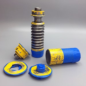 May include: A disassembled lightsaber with a blue and yellow paint scheme. The lightsaber is made of metal and has a textured surface. The lightsaber is in pieces, including the main body, a handle, and a cap.