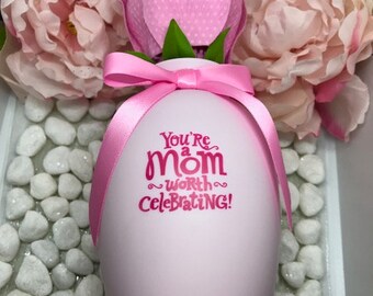 May include: A pink ceramic vase with a pink flower and a pink ribbon. The vase has the text "You're a mom worth celebrating!" printed on it.