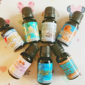 May include: Seven small glass bottles with black caps and colourful labels. The labels feature text and images related to Disney theme park attractions. The text on the labels includes "Magic Cruise Lobby", "Apple Orchard", "Smell the Street", "Mickey's Ohana", "Bakery Main Street", "A Flight of Fancy", and "Trader Sam's".