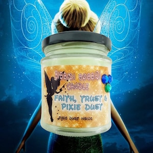May include: A green glass candle jar with a yellow label that reads "Bibbidi Bobbidi Candle, Faith, Trust & Pixie Dust, Pixie Dust Inside". The label has a cartoon fairy with a wand and sparkles. The jar has a black lid and is decorated with blue and green rhinestones.