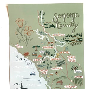 May include: A hand-drawn map of Sonoma County, California, with a green background and white lines. The map shows the locations of various towns and cities, including Santa Rosa, Sebastopol, Healdsburg, and Petaluma. The map also includes a compass, a whale, and a few other illustrations.