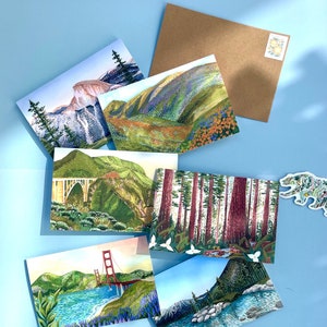 May include: Six illustrated postcards featuring various scenic landscapes. The postcards are arranged in a semi-circle on a light blue background. The postcards feature a variety of landscapes, including mountains, forests, and a bridge.
