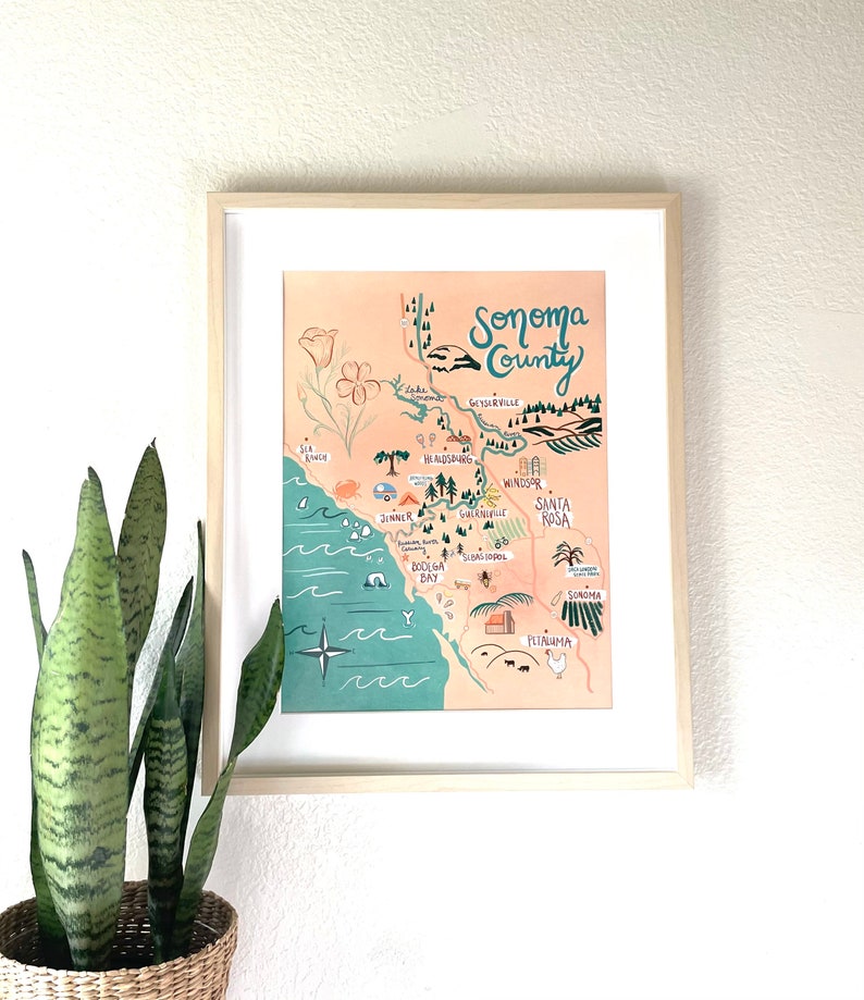 K&ouml;nnte beinhalten: Eine gerahmte Illustration einer Karte von Sonoma County, Kalifornien. Die Karte ist in einem skurrilen Stil mit handgezeichneten Schriftz&uuml;gen und Illustrationen von Sehensw&uuml;rdigkeiten, St&auml;dten und nat&uuml;rlichen Merkmalen gezeichnet. Die Karte befindet sich auf einem pfirsichfarbenen Hintergrund mit einem t&uuml;rkisfarbenen Rand.