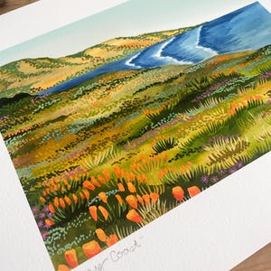 Peut inclure: Une peinture &agrave; l'aquarelle d'un paysage c&ocirc;tier avec une mer bleue en arri&egrave;re-plan et un champ de coquelicots orange au premier plan. Le texte "Poppy Coast" est &eacute;crit dans le coin inf&eacute;rieur droit de la peinture.