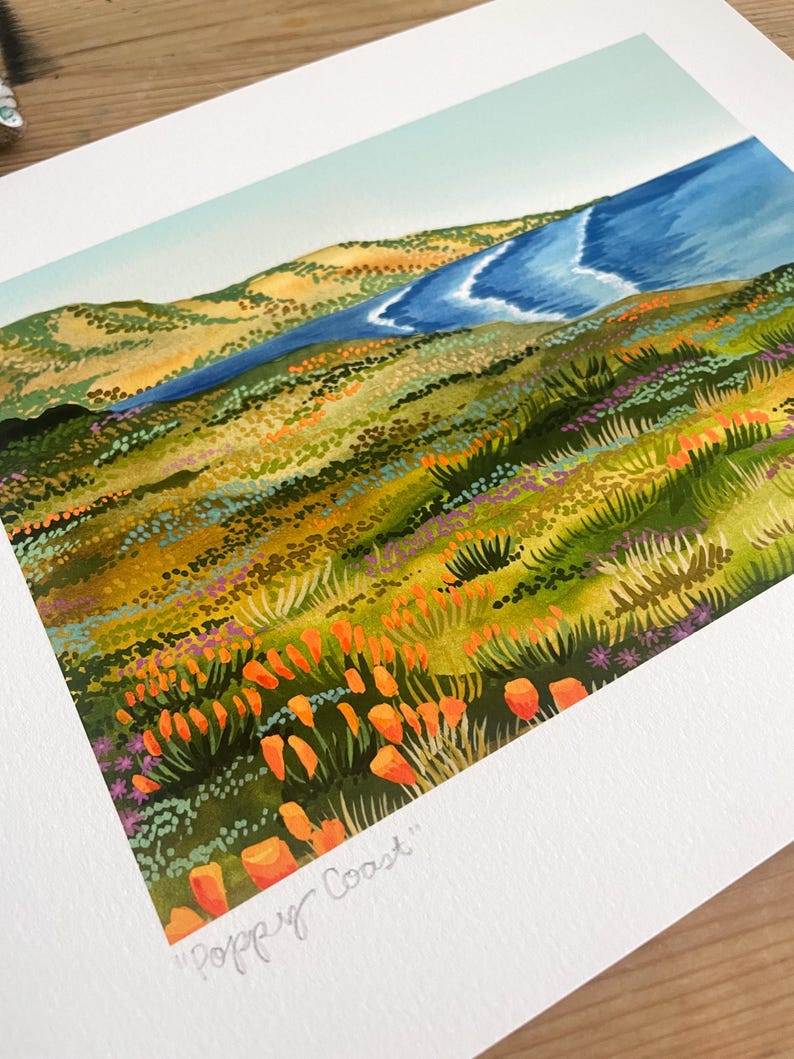 Peut inclure: Une peinture &agrave; l'aquarelle d'un paysage c&ocirc;tier avec une mer bleue en arri&egrave;re-plan et un champ de coquelicots orange au premier plan. Le texte "Poppy Coast" est &eacute;crit dans le coin inf&eacute;rieur droit de la peinture.