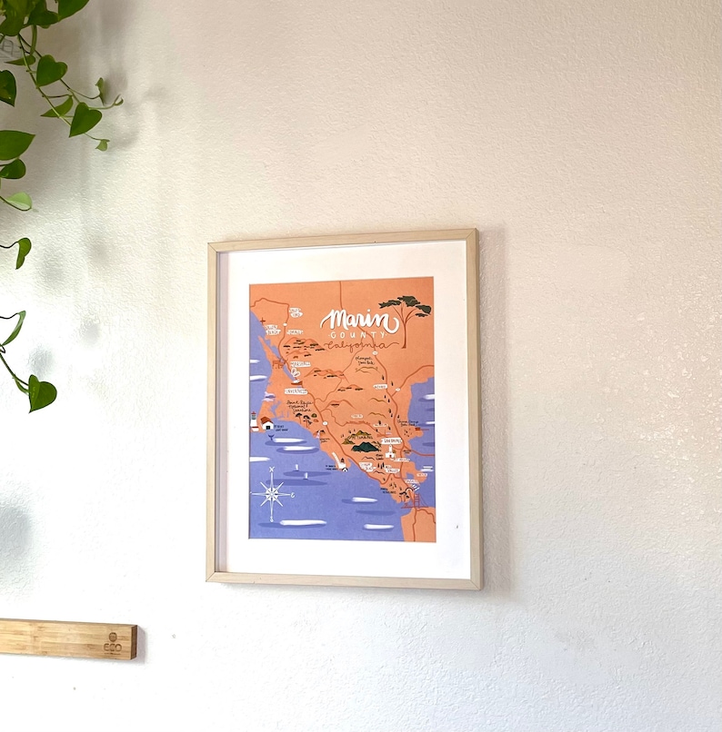 May include: A framed illustration of a map of Marin County, California. The map is in a light orange color with blue water and green trees. The text "Marin County, California" is written in white at the top of the map.