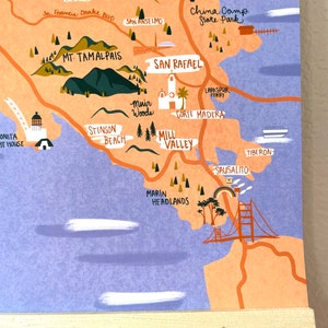 May include: A colorful illustrated map of the San Francisco Bay Area, showing various landmarks and locations, including Mt. Tamalpais, Muir Woods, Mill Valley, Marin Headlands, Sausalito, Tiburon, China Camp State Park, Corte Madera, Larkspur Ferry, and Stinson Beach. The map is drawn in a whimsical style with a light blue and peach background.