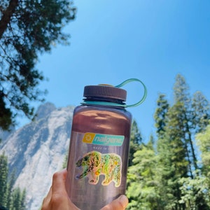 May include: A purple Nalgene water bottle with a floral bear sticker. The sticker says "nalgene" and "made in usa".
