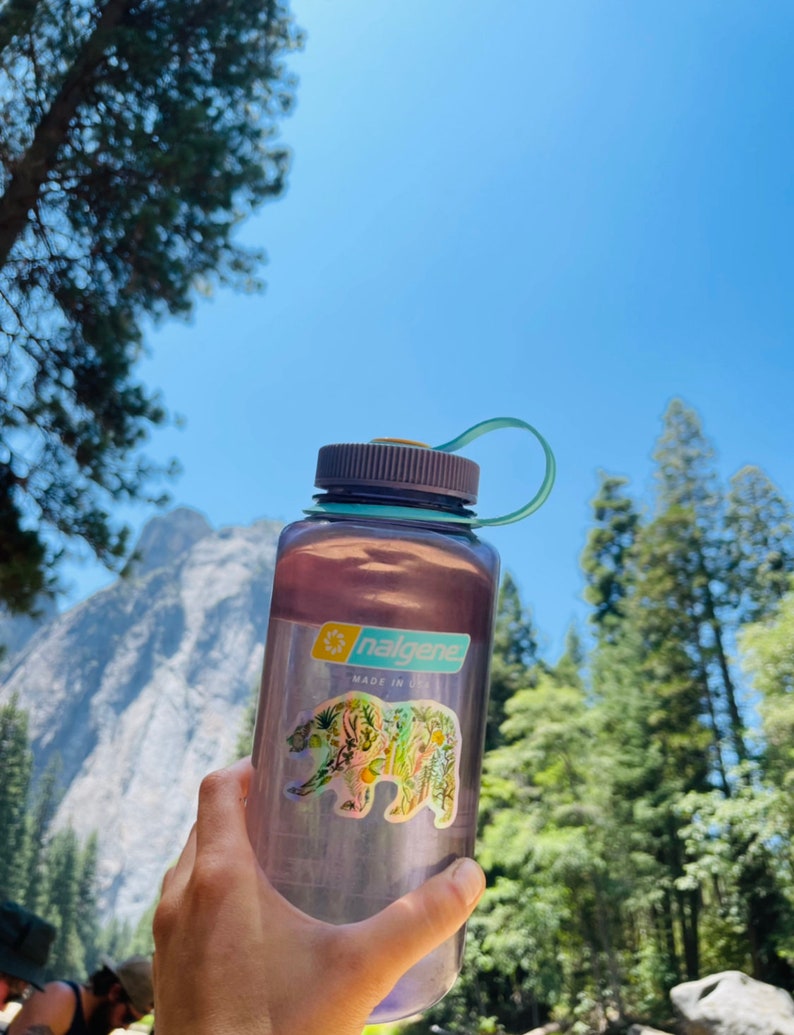 May include: A purple Nalgene water bottle with a floral bear sticker. The sticker says "nalgene" and "made in usa".