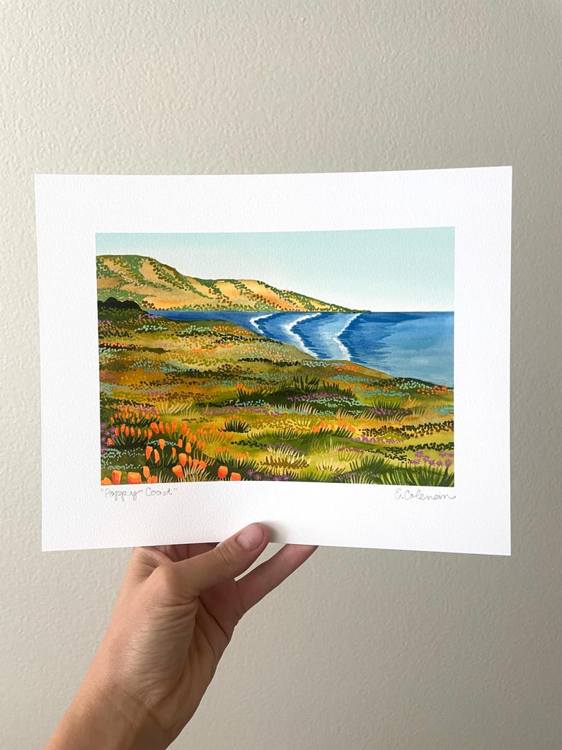 Peut inclure: Une peinture &agrave; l'aquarelle d'un paysage c&ocirc;tier avec une mer bleue, des collines verdoyantes et des fleurs sauvages orange. La peinture est sign&eacute;e "Poppy Coast" et "Coleman".