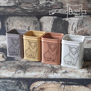 Peut inclure: Quatre contenants carrés en céramique dans les tons de gris, jaune, pêche et blanc. Chaque contenant présente un motif de renard géométrique en noir. Les contenants sont disposés en rangée, avec le texte "Le Boolot de Boo" visible.
