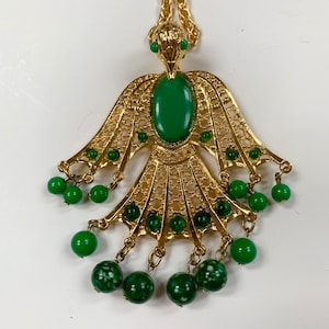 May include: A gold tone necklace with a green bird pendant and green beads. The bird has a filigree design and a large green stone in the centre.