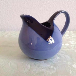 May include: A blue and dark blue ceramic creamer with a rounded body and a handle. The creamer has a glazed finish.