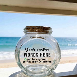 Peut inclure: Un bocal en verre transparent et rond avec un couvercle en liège. L'avant du bocal porte le texte noir : Your custom WORDS HERE, suivi d'une coche verte et du texte : can be engraved or full color uv-printed.