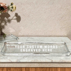 May include: A rectangular silver-toned glass tray with a textured surface featuring the white engraved text YOUR CUSTOM WORDS ENGRAVED HERE. The tray has slightly raised edges and a metallic finish, positioned horizontally on a flat surface.