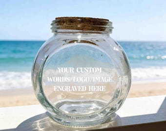 Könnte beinhalten: Ein klares, rundes Glasgefäß mit einem Korkstopfen. Auf der Vorderseite befindet sich eine weiße Gravur mit dem Text: YOUR CUSTOM WORDS/LOGO/IMAGE ENGRAVED HERE. Das Gefäß hat einen bauchigen Körper und einen kurzen, schmalen Hals.