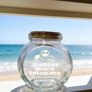 May include: A clear glass jar with a cork stopper featuring white etched graphics of a sun with sunglasses, a seashell, and stars. The text reads JESSICA'S BEACH TREASURES, JULY 2026, SEABRIGHT, NJ. The jar has a round body and a wide opening.