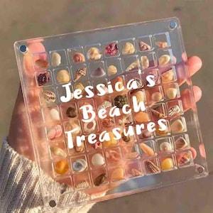 Könnte beinhalten: Ein quadratisches Display aus klarem Acryl mit einem Gitter aus einzelnen Fächern, die jeweils ein einzigartiges kleines Muschelgehäuse enthalten. Der weiße Text auf der Vorderseite des transparenten Gehäuses lautet Jessica's Beach Treasures.