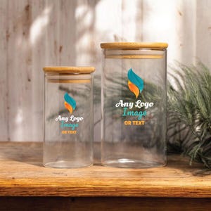 May include: Two clear glass jars with bamboo lids. The jars have a logo with blue, orange, and teal colors and the text "Any Logo Image OR TEXT". The jars are on a wooden surface.