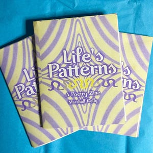 Op de afbeelding: Drie exemplaren van een poëziezine getiteld "Life's Patterns" worden getoond. De omslag heeft een geel en paars abstract ontwerp met de titel in witte en paarse letters. De naam van de auteur, Marshall Kelly, is ook zichtbaar.