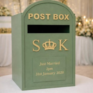 Puede incluir: Una caja de correo verde salvia con la inscripci&oacute;n "POST BOX" en letras doradas. La caja presenta las iniciales "S & K" con una corona y el texto "Just Married 2pm 31st January 2020".