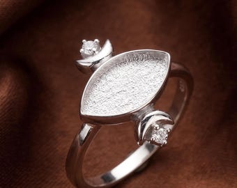 Op de afbeelding: Een zilverkleurige ring met een centrale markiesvormige zetting met een getextureerde, matte afwerking. De zetting wordt geflankeerd door twee kleine, halvemaanvormige accenten, elk bekroond met een enkele, heldere, rond geslepen steen.