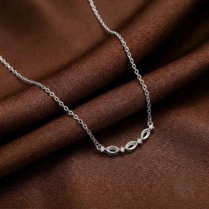 May include: A silver-toned necklace featuring a delicate chain and a central pendant composed of three interconnected marquise-shaped links, each accented with a small, clear, round-cut stone set within the metal frame.