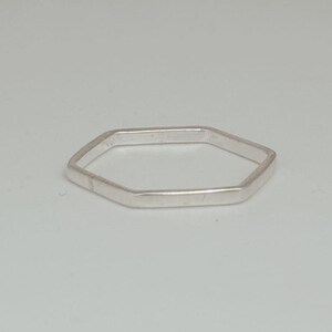 May include: A silver-colored ring with a geometric, hexagonal design. The ring is simple and minimalist, with a polished finish. The ring is a piece of jewelry.
