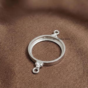 May include: A silver-colored, circular jewelry finding with two small loops and a decorative cluster of beads. The text "Gem finding World" is visible on the image. The finding is designed to hold a round stone or other element.