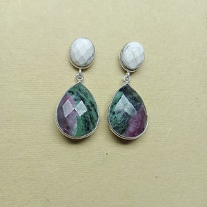 Puede incluir: Un par de pendientes de plata con una piedra ovalada blanca en la parte superior y una piedra facetada en forma de lágrima debajo. La piedra inferior es una mezcla de colores verdes, rojos y claros.