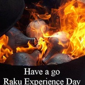May include: A close-up of pottery pieces inside a kiln engulfed in flames. The image shows a Raku firing process, with bright orange and yellow flames surrounding the ceramic objects. Text at the bottom reads "Have a go Raku Experience Day."