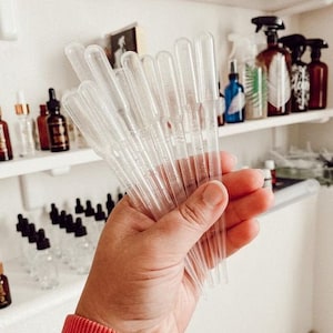 May include: A hand holding a bunch of clear plastic droppers. The droppers are used for dispensing liquids.