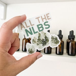 May include: A white sticker with the text "ALL THE NLBS" in brown and green lettering. The sticker features a watercolor illustration of a cluster of green trees.