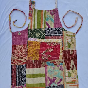 May include: A patchwork apron with a variety of colorful fabric squares. The apron features a neck strap and waist ties. The design includes floral, striped, and geometric patterns in shades of red, pink, green, yellow, and blue.