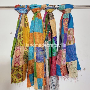 May include: Three colourful patchwork scarves made of kantha fabric. The scarves are hanging from a rod and are made of a variety of fabrics in shades of blue, green, orange, yellow, and red. The scarves are all different sizes and have a variety of patterns.