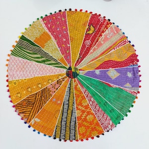 May include: Circular patchwork textile with a vibrant array of colors and patterns. The design features pieced fabric sections radiating from a central point, with a border of colorful pom-poms. The textile showcases a variety of textures and designs.
