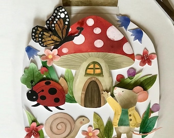 Op de afbeelding: Een papieren collage in de vorm van een pot met een rood-wit paddenstoelhuisje, een bruine muis in een geel jasje, een zwart-oranje vlinder, een rood lieveheersbeestje met zwarte stippen, een beige slak en diverse kleurrijke bloemen en groene bladeren.