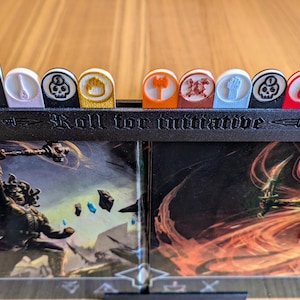 May include: A black plastic initiative tracker with a row of colourful tokens. The tokens have different symbols, including a dragon, a sword, a skull, a house, a hammer, a skull and crossbones, a fist, a drop of blood, and a sword. The text "Roll for initiative" is printed on the tracker.