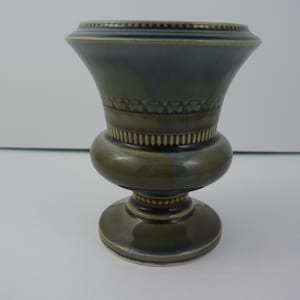 May include: A green and blue ceramic vase with a decorative design around the middle. The vase has a wide base and a narrow neck.