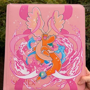 May include: A pink binder featuring a central orange dragon-like creature with wings, surrounded by smaller blue and pink dragon figures, swirling ribbons, and white star accents. The word vaultx is printed in the bottom left corner in pink text.
