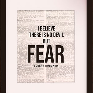 Könnte beinhalten: Schwarz-weißes Typografie-Druck mit dem Zitat "Ich glaube, es gibt keinen Teufel, sondern nur Angst." von Elbert Hubbard. Der Druck ist in einem schwarzen Rahmen gerahmt und an einer roten Backsteinwand ausgestellt.