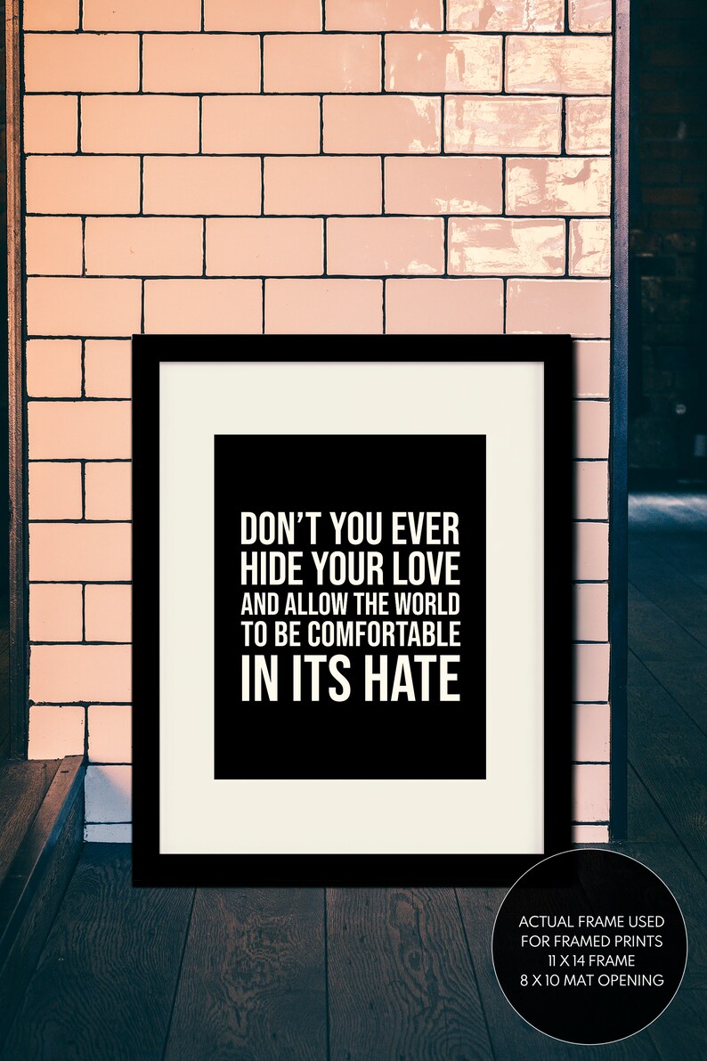 Puede incluir: Impresi&oacute;n tipogr&aacute;fica en blanco y negro con la cita "Nunca escondas tu amor y no permitas que el mundo se sienta c&oacute;modo en su odio." La impresi&oacute;n est&aacute; enmarcada en un marco negro con un passe-partout blanco. El marco mide 28 x 36 cm y la abertura del passe-partout es de 20 x 25 cm.