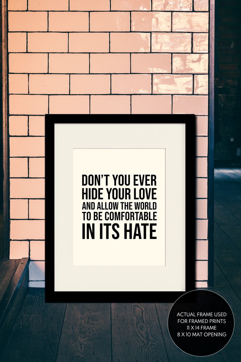 Puede incluir: Impresi&oacute;n tipogr&aacute;fica en blanco y negro con el texto "Don't you ever hide your love and allow the world to be comfortable in its hate". La impresi&oacute;n est&aacute; enmarcada en un marco negro y se muestra contra una pared de azulejos rosas. El marco real utilizado para las impresiones enmarcadas es de 28 x 36 cm y la abertura del passe-partout es de 20 x 25 cm.