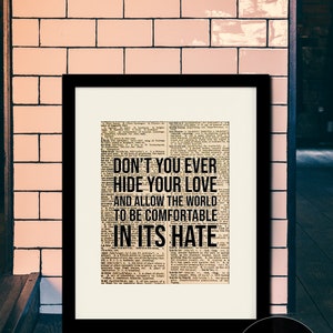 Puede incluir: Una impresi&oacute;n enmarcada en negro con un fondo de peri&oacute;dico vintage que presenta el texto "Don't you ever hide your love and allow the world to be comfortable in its hate". La impresi&oacute;n est&aacute; enmarcada con un marco y un passe-partout negros, y el tama&ntilde;o real del marco es de 28 x 35,5 cm con una abertura de passe-partout de 20,3 x 25,4 cm.