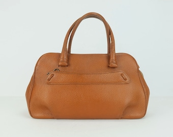 May include: A brown leather handbag with two top handles. The bag has a flap closure and a small pocket on the front.