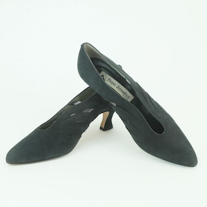 May include: A pair of dark green suede heeled shoes with cutouts. The shoes have a pointed toe and a small heel. The brand name "Pepe Jimenez" is printed on the side of one shoe.