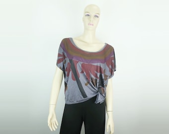 Op de afbeelding: Een grijs, kort mouwig shirt met een kleurrijke abstracte print. Het shirt heeft een ronde hals en is aan de voorkant geknoopt.