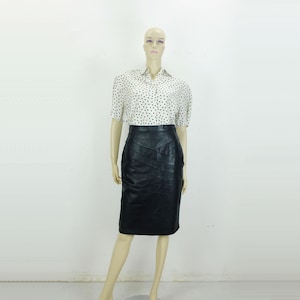 Könnte beinhalten: Ein schwarzer Lederrock mit gerader Silhouette und einem Panel-Design. Der Rock ist knielang und hat eine hohe Taille.