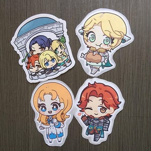 Puede incluir: Cuatro pegatinas de dibujos animados con personajes de estilo anime. Una muestra un grupo bajo un arco. Las otras tres representan personajes individuales con cabello rubio, naranja y rojo, cada uno con atuendos y expresiones &uacute;nicos. Las pegatinas est&aacute;n sobre una superficie gris.